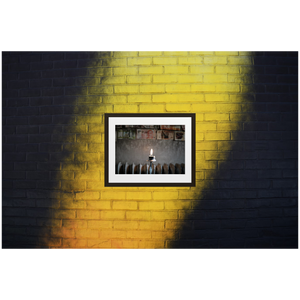 Framed Photo Print Poster "Flame Of Hope" on black and yellow brick wall. Shows a burning candle with different currency bills in the background. Shot at a cafe is Stockholm. Photography by Jacob Sellström. Printed on matte paper with wooden frame. Two sizes: 8x10, 12x16.