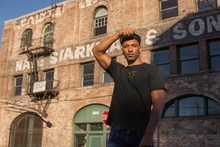 Guy in New York City, urban setting, is wearing black & yellow t-shirt with "RIF" Roast In Focus logo. Comfortable cotton. Sizes S-XL. Logo collection.