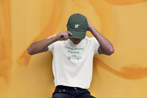 Guy leaning on yellow wall waering "a vintage lifestyle & coffee to fuel it" T-shirt and green embroidered dad hat with "RIF" Roast In Focus logo. Vintage feel, one size unisex cap.